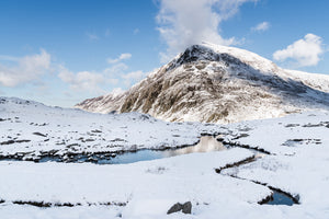 The Snowy Stream to Pen yr Ole Wen, Snowdonia - North Wales. A thick layer of snow lays on the ground at Cwm Idwal looking towards Pen yr Ole Wen with blue skies and cloud
