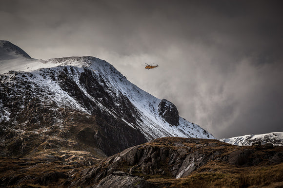 RAF Mountain rescue in Snowdonia. The now retired, yellow Seaking helicopter flies around the snow covered mountains surrounding llyn Idwal